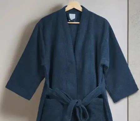 A soft navy bathrobe hanging in the room, collar to the tied belt