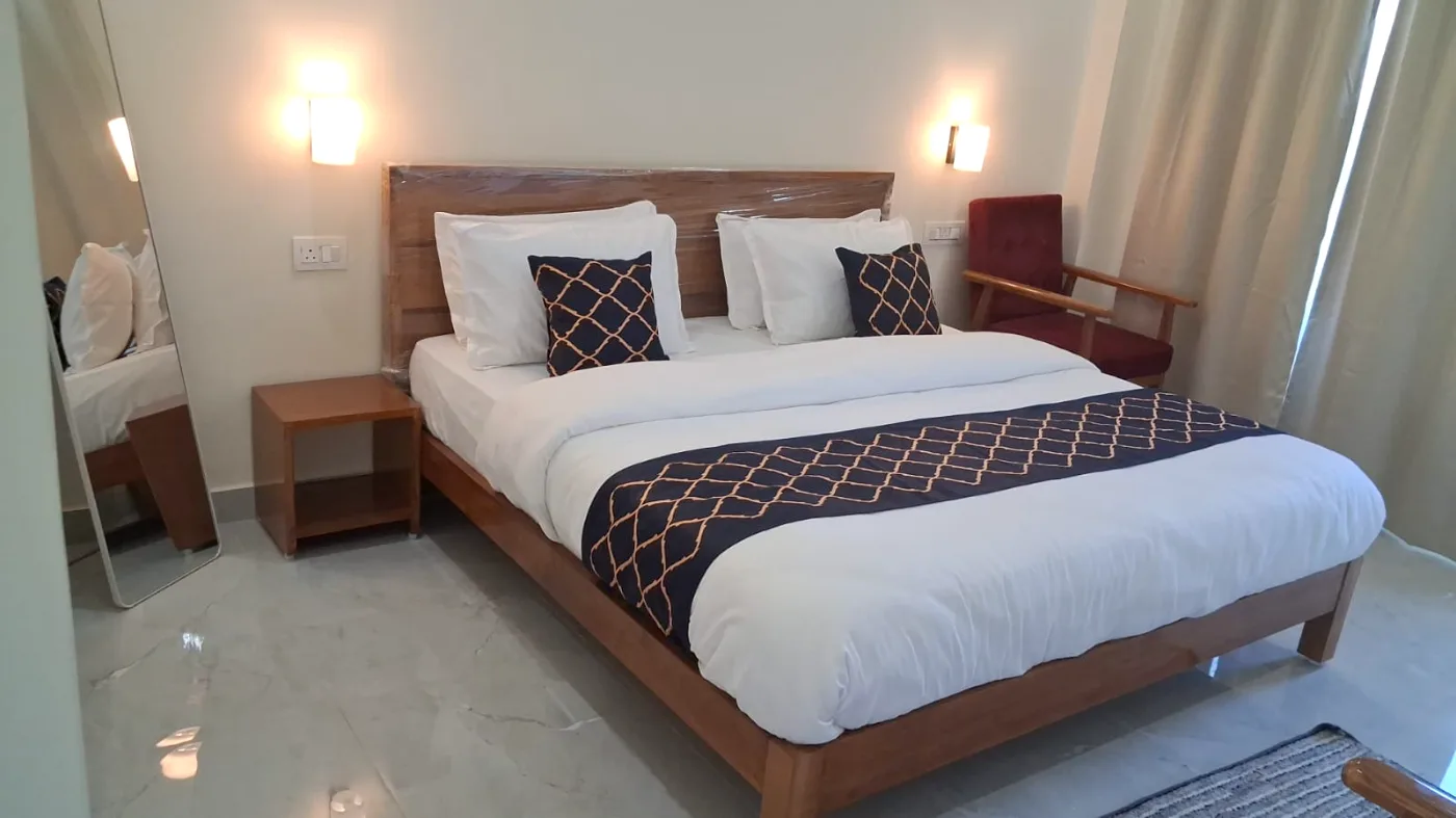 King bed dressed in white linen with navy and gold cushions, warm wall sconces, a lounge chair and full-length mirror